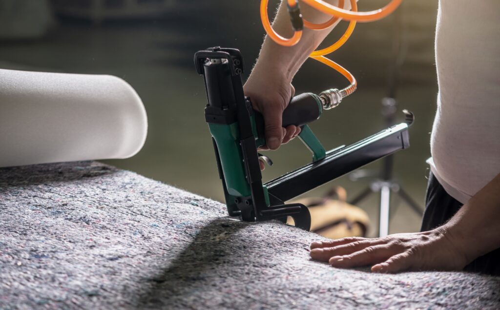 employee-holds-his-hands-industrial-air-stapler-sheathe-soft-fabric-upholstery-closeup-min - carpet vs area rug cleaning bellevue wa