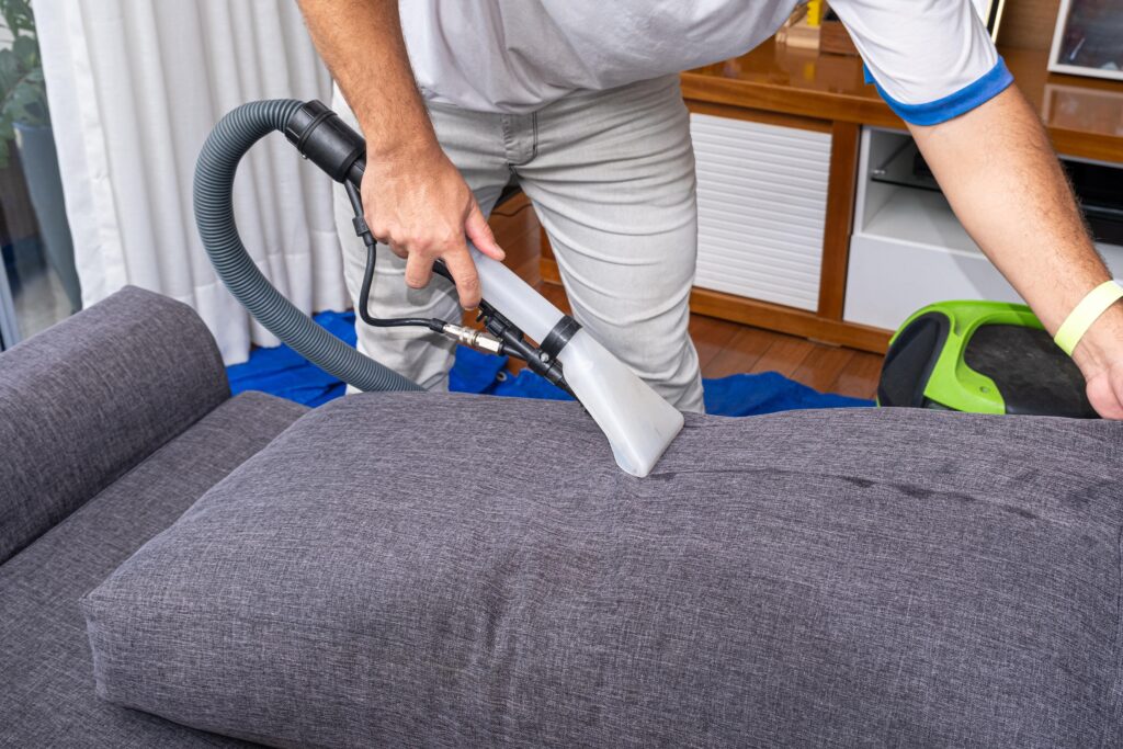 man-using-special-vacuum-clean-gray-sofa-cushionsside-view-min